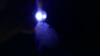 Somebody with a hand lamp found a fingerprint left on a dark surface and lightens it up...