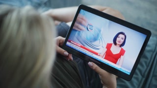 Close up of Caucasian woman watching breaking news about US presidential elections using tablet computer while relaxing on sofa.