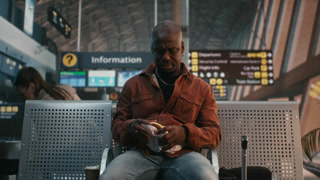 Man Takes Break From Journey Have Quick Snack. Sitting in Airport Waiting Area With Luggage Nearby, Male Unwraps Sandwich and Drinks Coffee
