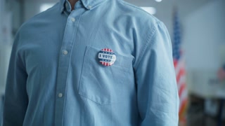 Anonymous Caucasian male voter or businessman puts on badge with American flag logo and inscription I Voted. US citizen at polling station
