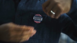 Anonymous African American man puts on badge with USA flag logo and inscription I Voted. US citizen at polling station during elections