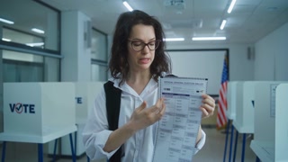 American female voter looks and speaks on camera, shows paper ballot, calls for voting. National Election Day in the United States. Voting