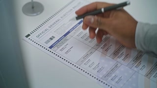 Close up of anonymous US citizen choosing which presidential candidate to vote for in paper ballot in voting booth. African American man at