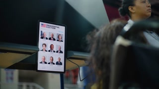 US female voter with physical disability looks at tablet computer for voting. Woman with SMA in wheelchair votes in voting booth at polling