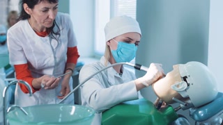 Dentistry student or hygienist practicing on a dummy at a medical school as a qualified teacher demonstrates the technique to her from behind