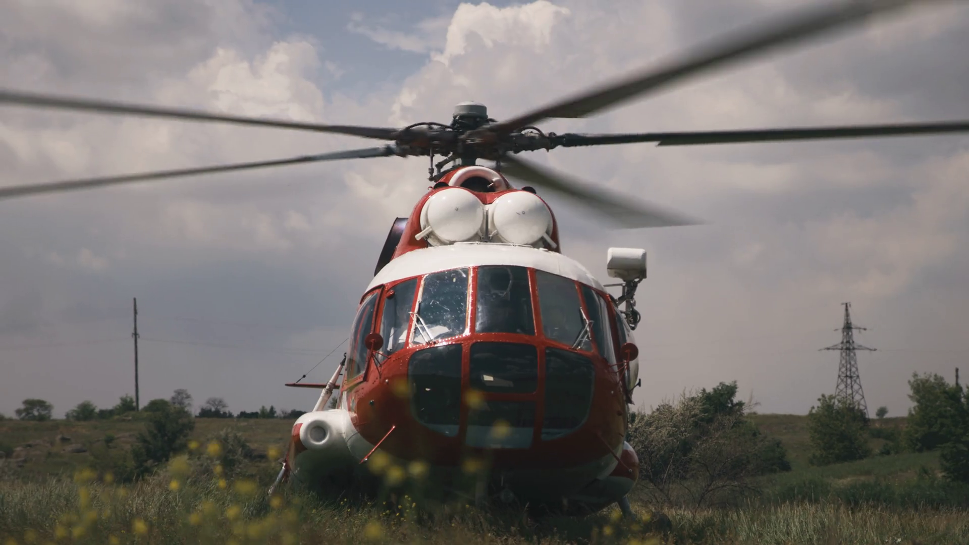 Red and white helicopter with rotating propeller landed in grassy field