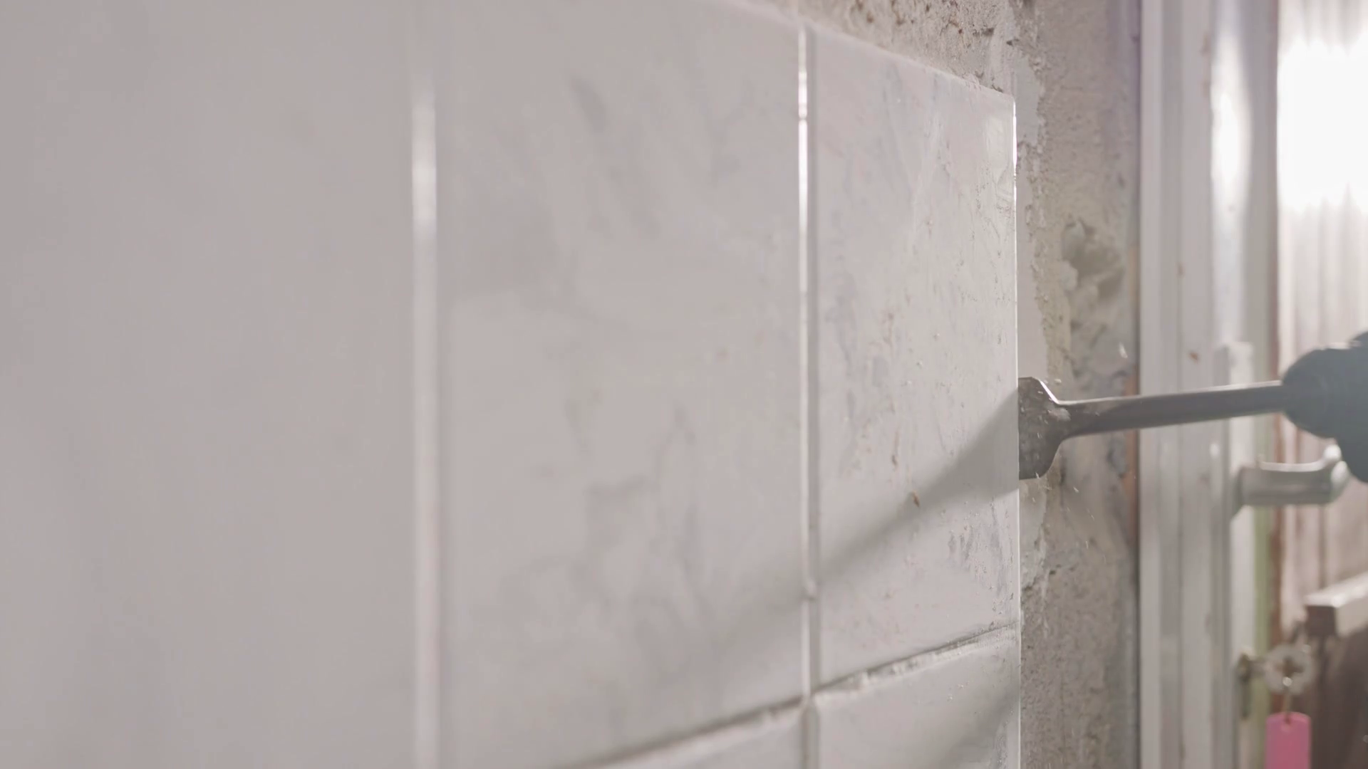 Slow motion of a rotary hammer breaking ceramic tiles off a wall Stock