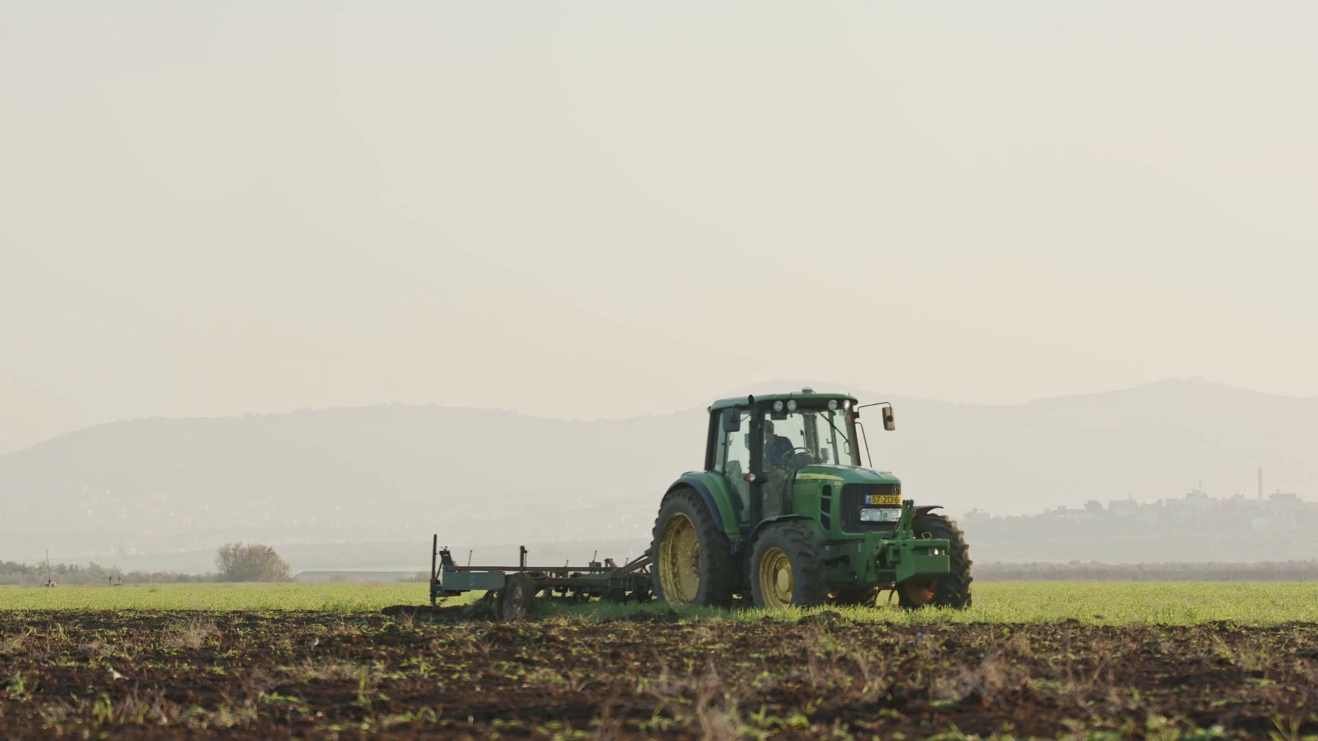 Tractor cultivating a green field in slow motion. Stock Video Footage