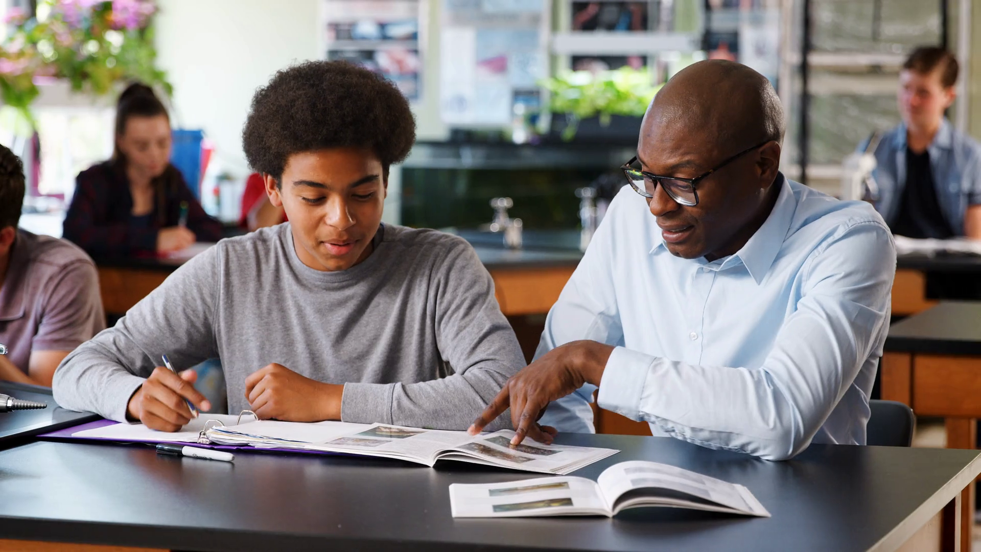 High School Tutor Sitting At Desk With Male Student In Biology Class