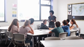 Female High School Tutor Standing By Table With Students Teaching Lesson