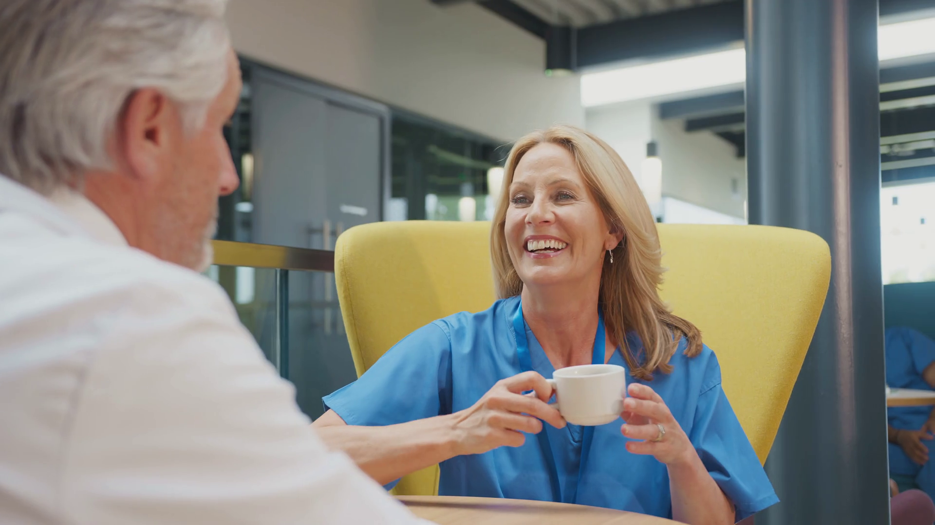 Two Medical Staff In White Coat And Scrubs Taking A Break And Talking