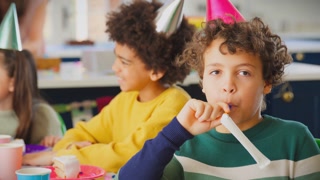 Boy With Birthday Cake And Party Blower At Party With Parents And Friends At Home