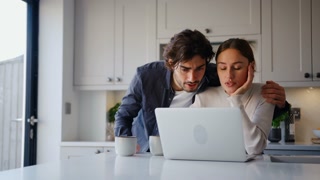 Young Couple At Home With Woman At Counter Working On Laptop And Man Bringing Her Hot Drink