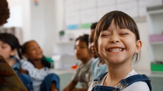 Portrait Of Female Elementary School Pupil With Teacher Reading To Class In Background