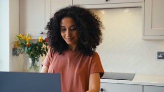 Young Woman At Home Working On Laptop On Kitchen Surface