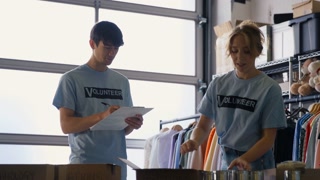 Male And Female Charity Volunteers Working Sorting Through Donations Of Food And Clothing