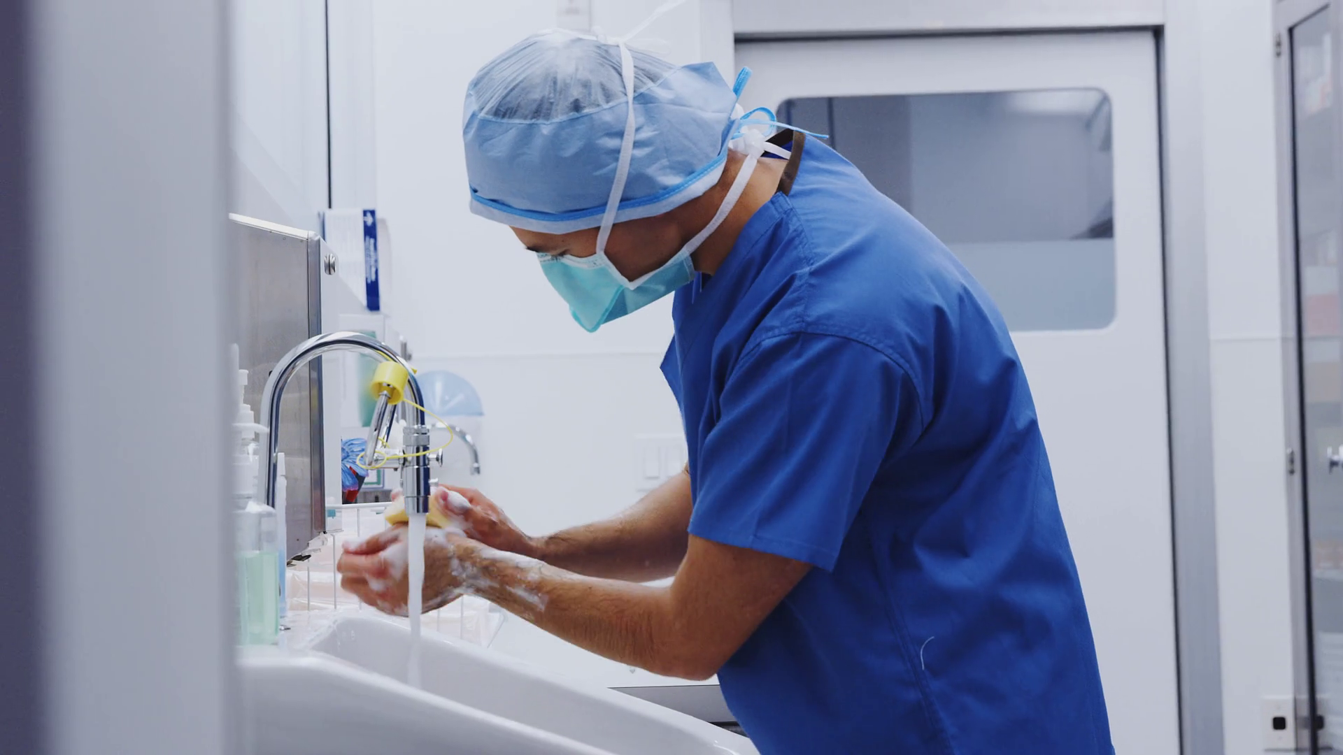 Male Surgeon Wearing Scrubs Washing Hands Before Operation In Hospital