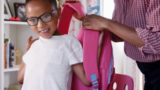 Mother Helping Daughter To Pack Bag For School In Bedroom