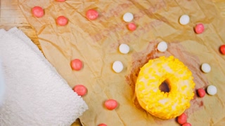 Pink donuts decorated with yellow icing. Donuts are on a piece of paper decorated with candy. Macro and slider shooting. The candies move in slow motion