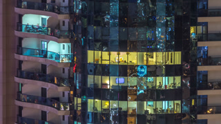 Windows of the multi-storey building of glass and steel lighting inside and moving people within timelapse