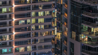 Rows of glowing windows with people in apartment building at night.