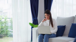 Young asian woman using laptop while seated on couch at home