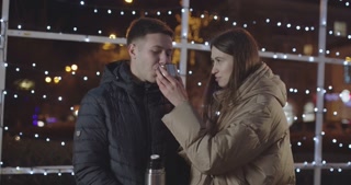 Young man enjoys hot tea with his partner on a chilly evening stroll