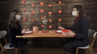 Couple in medical masks clinking glasses of champagne and exchanging valentine presents Covid 19, quarantine, infection of coronavirus