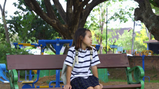 Cute Asian student girl sitting on a wooden bench and waiting for the bus after school, Back to school and childhood lifestyle concept.