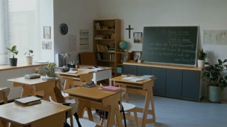No people shot of empty classroom with single school desks and chairs in modern religious school with Cristian cross on wall and Bible quotes on blackboard