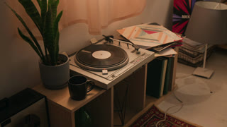 Vintage turntable spinning vinyl record on wooden shelf next to potted plant and mug. Visual for retro lifestyle commercials, music store advertisements, or home decor marketing campaigns