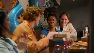 Surprised and excited young birthday man hugging and thanking his friends for presents, celebrating in bar