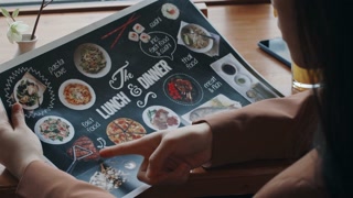 Close-up shot of unrecognizable woman holding menu with images of dishes and choosing what to eat in restaurant