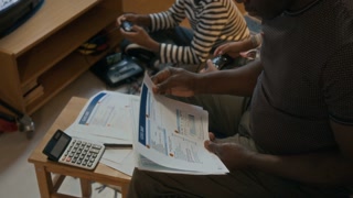 High angle shot of unrecognizable poor African American man looking through past due bills, while his children playing games in retro console