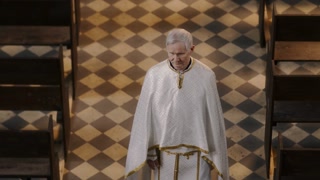 High angle shot of senior pastor with grey hair wearing chasuble going through cathedral