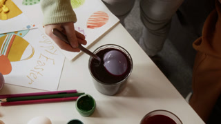 High angle cropped shot of hand of unrecognizable child taking out dyed egg from glass filled with liquid food coloring, preparing for Easter celebration at home