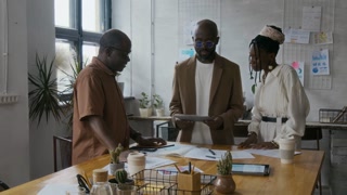 African American man in smart casual clothes joining two of his colleagues during business meeting in bright modern office