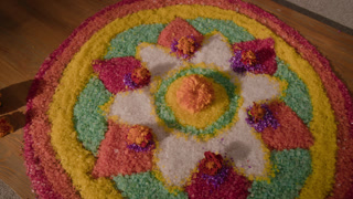 Colorful decorative sand mandala with marigold flowers lying on wooden floor, shot from high angle. Footage suitable for cultural heritage projects, holiday greetings, and festival promotions