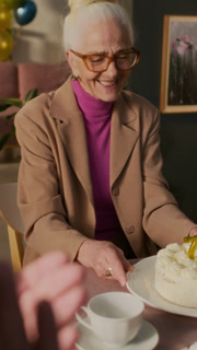 Vertical view of senior woman putting cake in front of excited lady blowing candles out on her 70th birthday