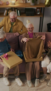 Vertical high angle view of elegant senior woman opening presents given to her by elderly friends for birthday during celebration in home setting