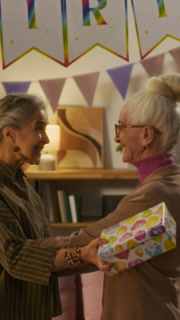Vertical view of three elderly guests arriving at birthday party of their female friend with gifts, they warmly greeting her and walking into living room
