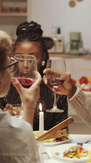 Vertical view of multi-ethnic friends clinking glasses in toast while having dinner during home party