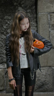 Portrait of Asian teenager girl in Halloween makeup looking at camera while holding carved pumpkin. Clip is ideal for seasonal holiday marketing and youth lifestyle advertisements, vertical