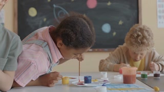 Little African American girl mixing paint in palette while drawing picture during art class in school