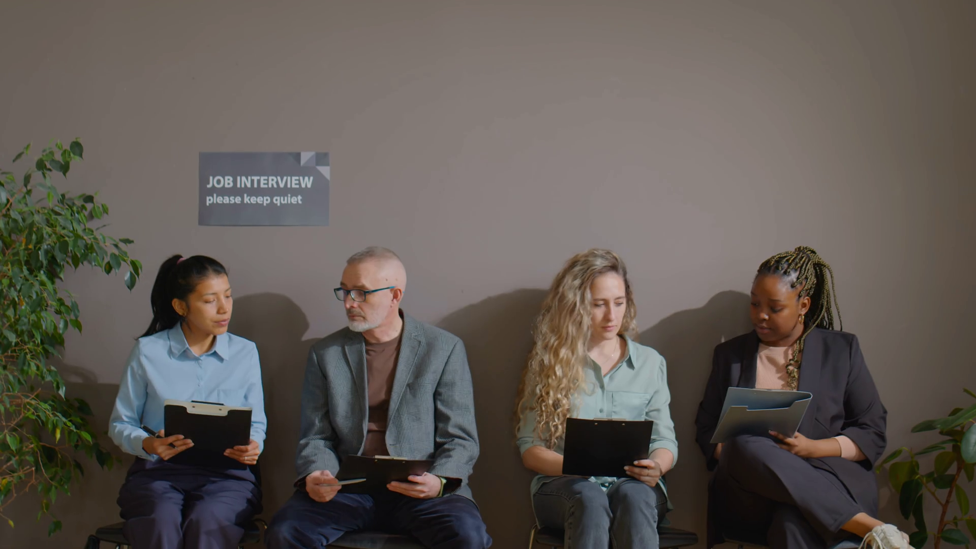Zoom in shot of multiethnic men and women sitting with clipboards in office corridor and