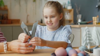 Cheerful mother and daughter decorating Easter egg at home