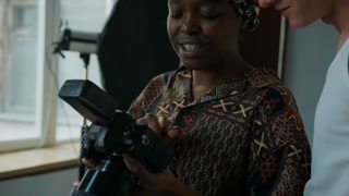 Close up view of African American female photographer showing photos on digital camera and having talk with young male model after studio shoot