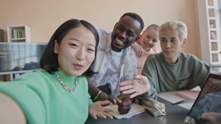 POV shaky cam shot of group of cheerful diverse students sitting in college classroom, smiling and chatting on camera during video call or live stream