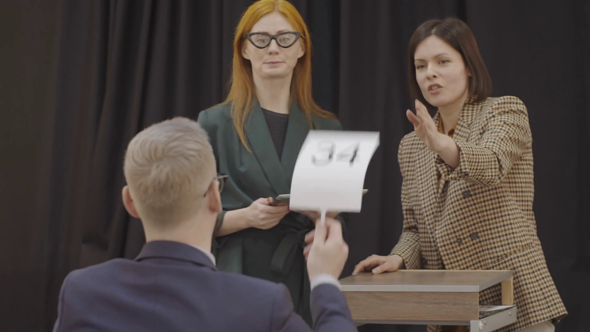 female auctioneer standing at lectern beside colleague, pointing at