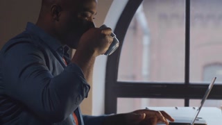 Young man working on laptop near arch window, enjoying coffee